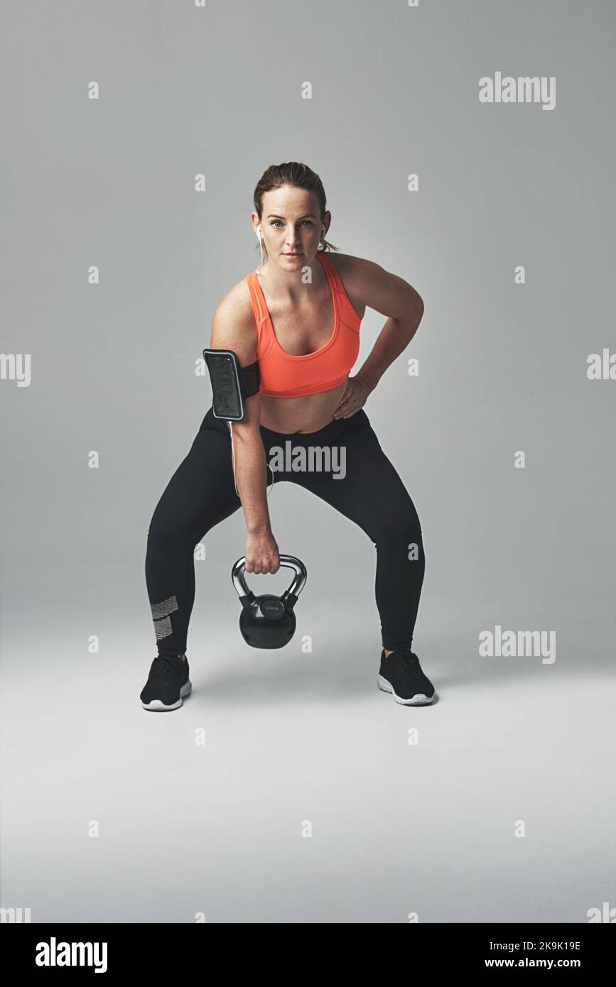 Es wird immer fitter, und zwar jeweils ein Vertreter. Studioporträt einer athletischen jungen Frau, die mit einer Kesselglocke vor grauem Hintergrund trainiert. Stockfoto