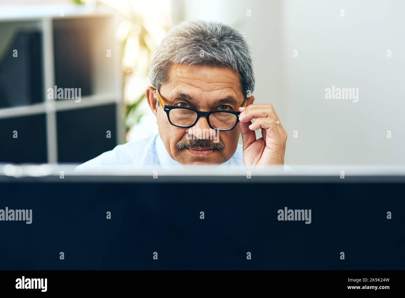 Er sieht ein wenig besorgt aus. Ein fokussierter reifer Mann, der tagsüber an einem Computer arbeitet, während er an einem Schreibtisch in einem Gebäude sitzt. Stockfoto