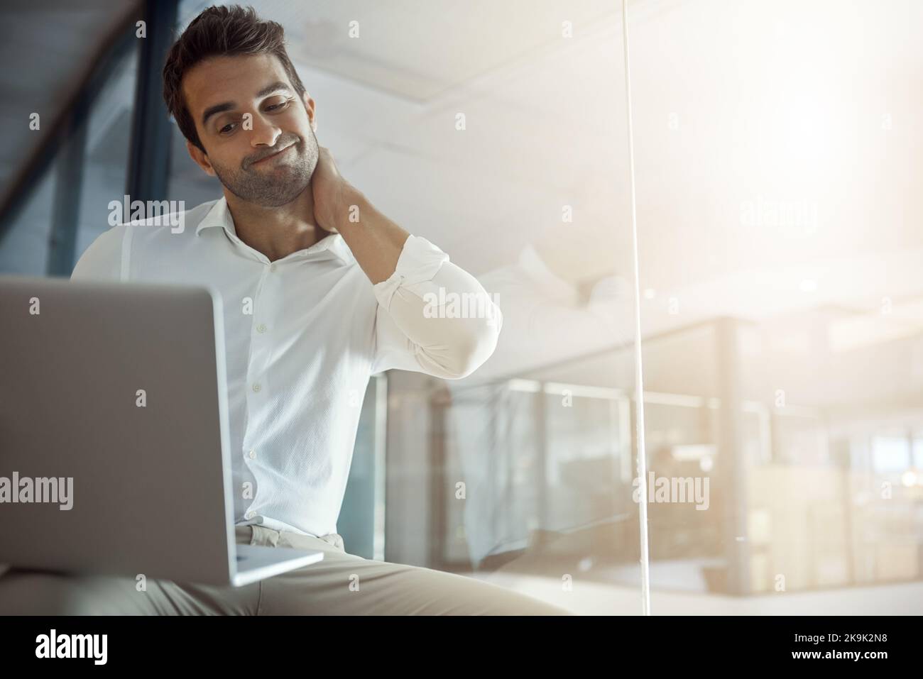 Ein hübscher junger Geschäftsmann sieht unsicher aus, während er im Büro an seinem Laptop arbeitet. Stockfoto