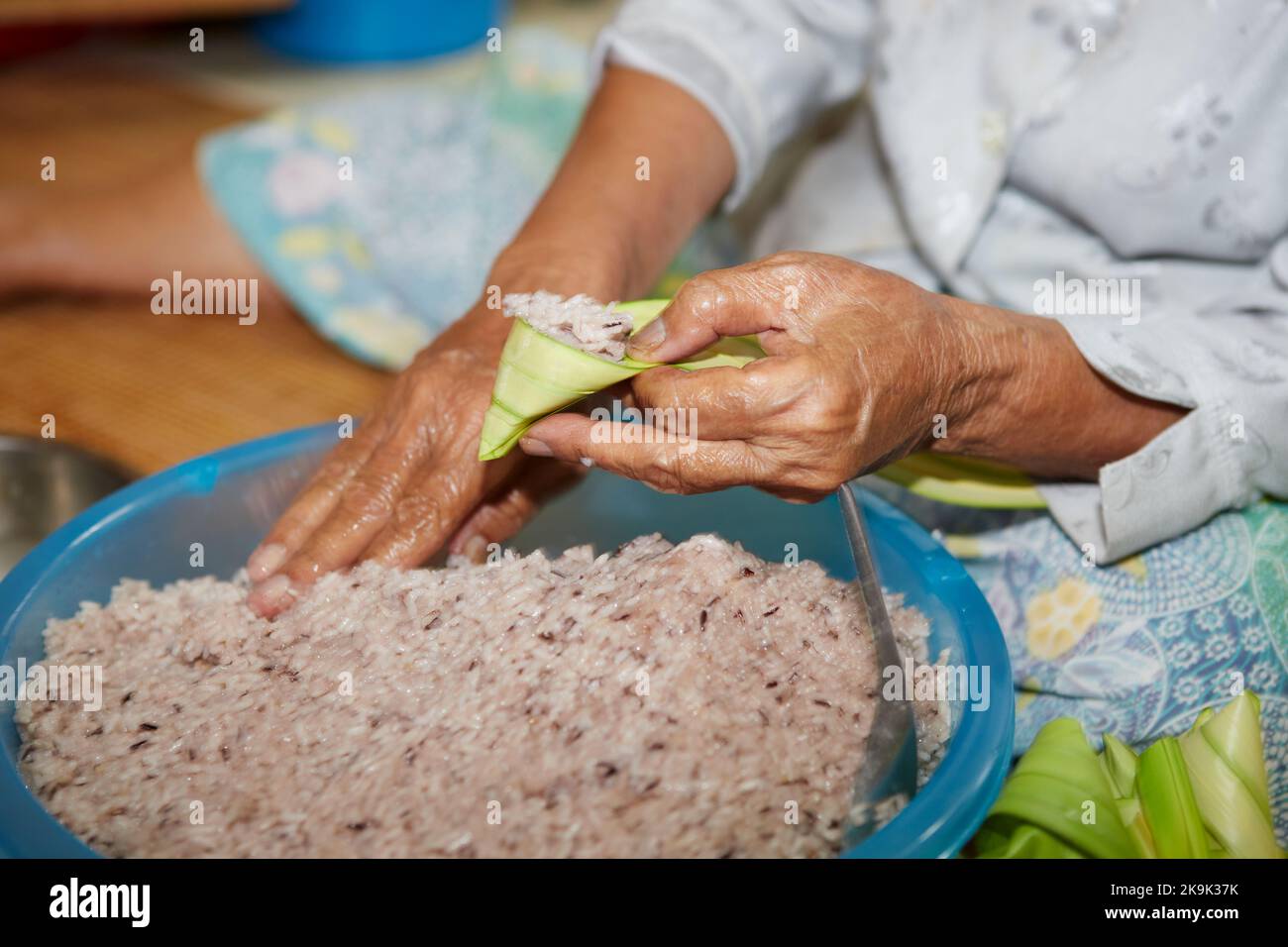 Hände einer älteren Frau, die den klebrigen Reis mit Palmblatt oder Ketupat Palas umwickelt Stockfoto