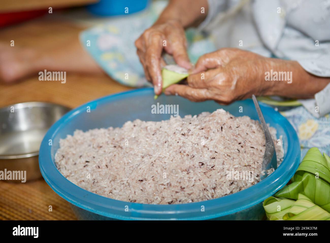 Hände einer älteren Frau, die den klebrigen Reis mit Palmblatt oder Ketupat Palas umwickelt Stockfoto
