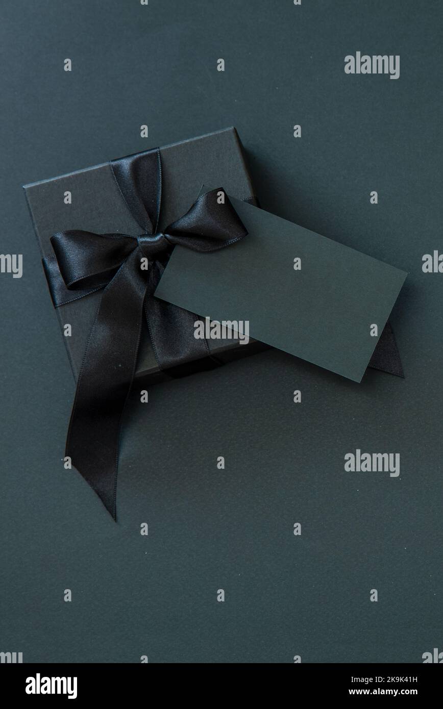 Geschenkbox mit schwarzem Band und leerer Karte isoliert vor schwarzem Hintergrund, Black Friday Sale und Weihnachtsgeschenke. Stockfoto