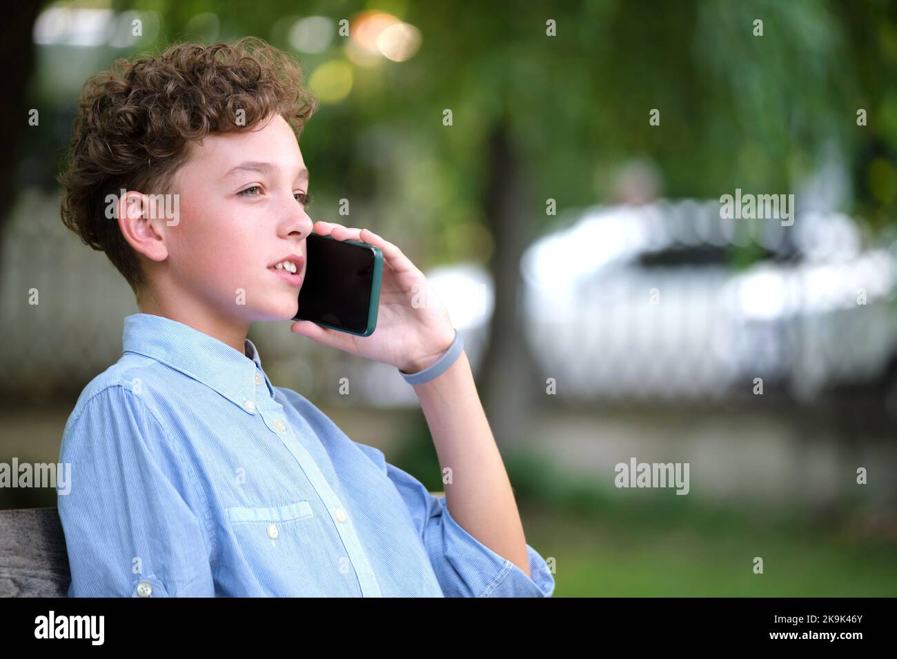 Kleiner Junge, der im Sommerpark mit dem Handy im Gespräch ist. Konfliktsituationen im Teenageralter Konzept. Stockfoto