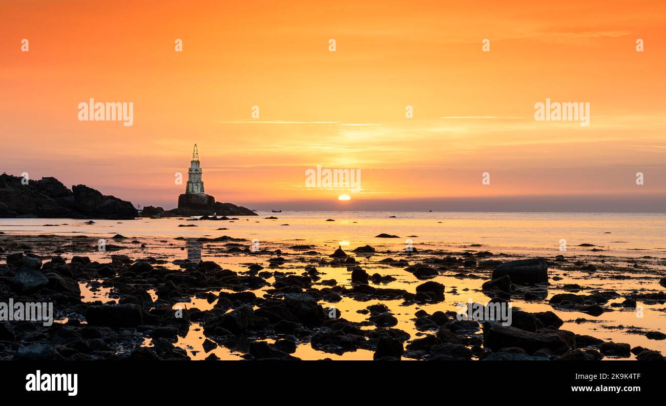 Landschaft des Sonnenaufgangs an der bulgarischen Schwarzmeerküste in Atopol mit dem Hafen Leuchtturm und felsigen Ufer Stockfoto