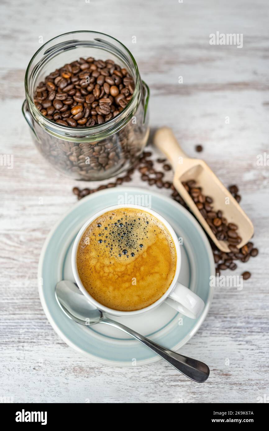 Frisch gebrühter Kaffeebecher und Glas mit gerösteten Kaffeebohnen auf einem Vintage-Tisch. Stockfoto