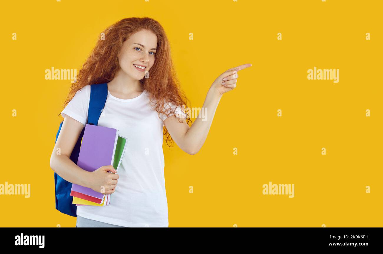 Schöne Studentin pochend mit ihrem Zeigefinger auf die rechte Seite, isoliert auf orangenen Hintergrund Stockfoto