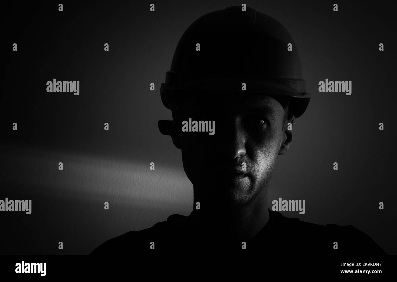 Schmutziges Gesicht des Kohlebergarbeiters auf schwarzem Hintergrund. Kopf eines müden Bergarbeiters in einem Hut. Stockfoto