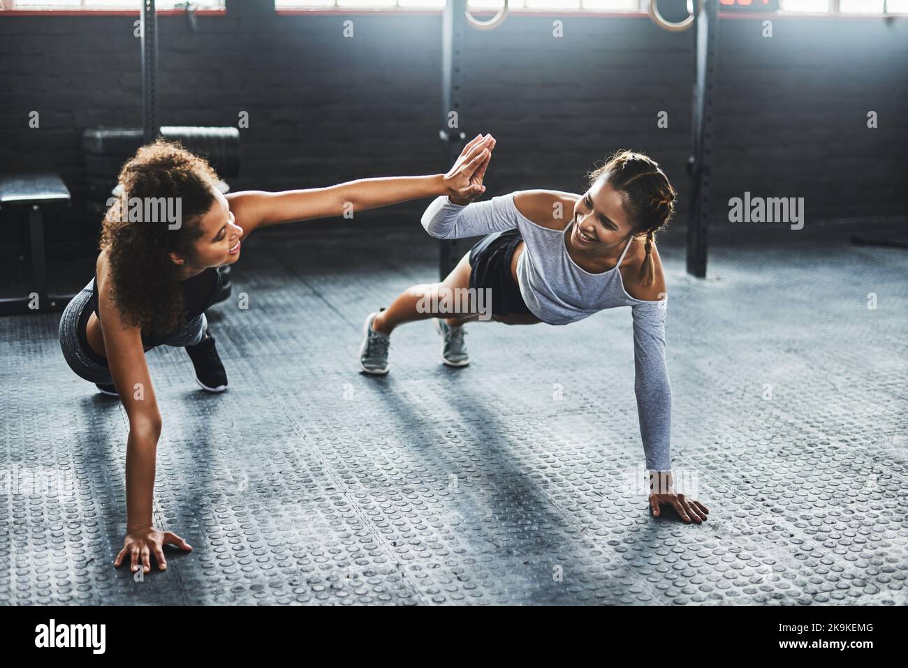 Die besten Freunde sind die besten Motivatoren. Zwei junge Frauen geben sich gegenseitig eine hohe fünf, während sie Liegestütze im Fitnessstudio machen. Stockfoto