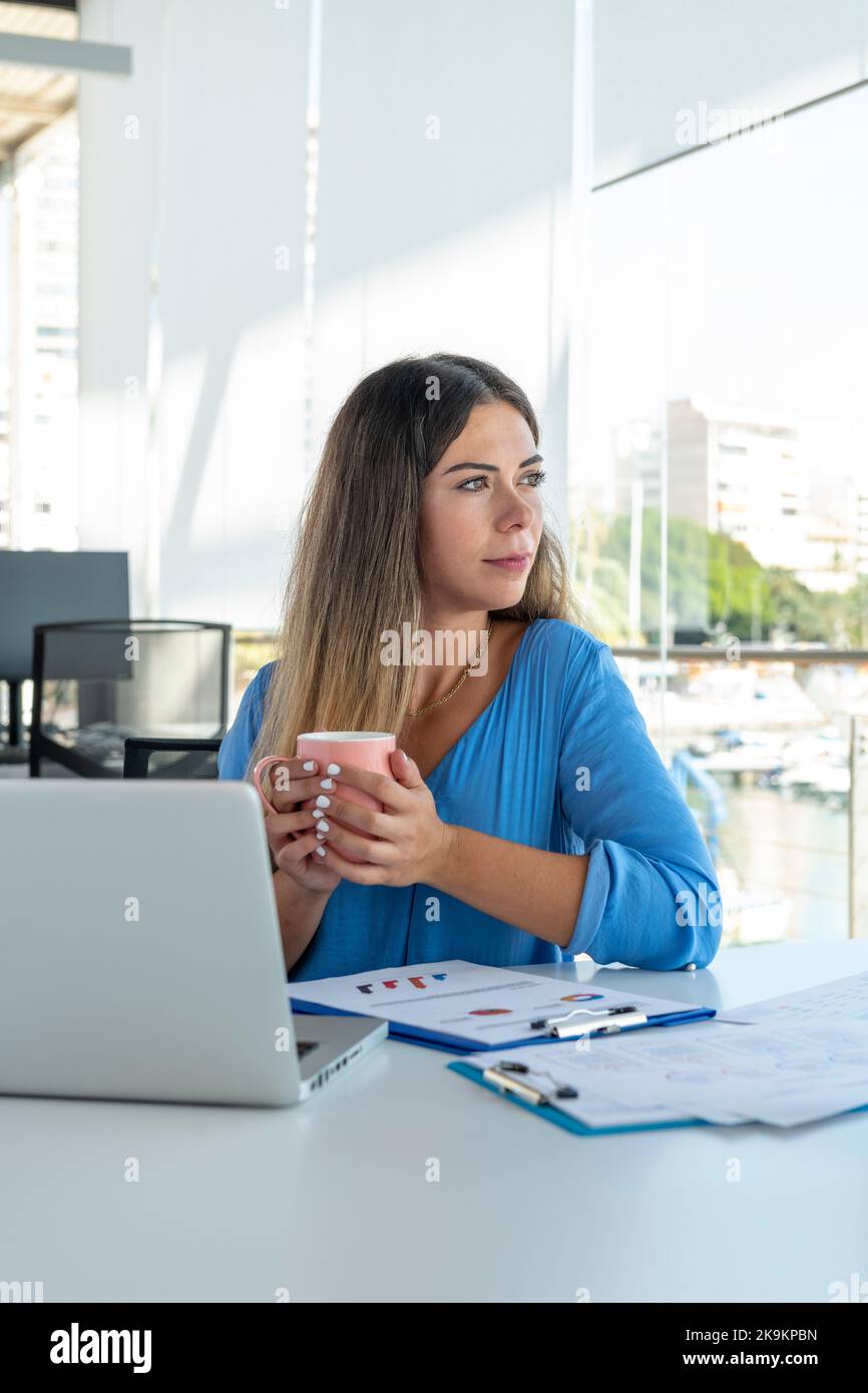Junge Geschäftsfrau auf einem Laptop im Büro mit einer durchdachten Haltung - Stock Foto Stockfoto