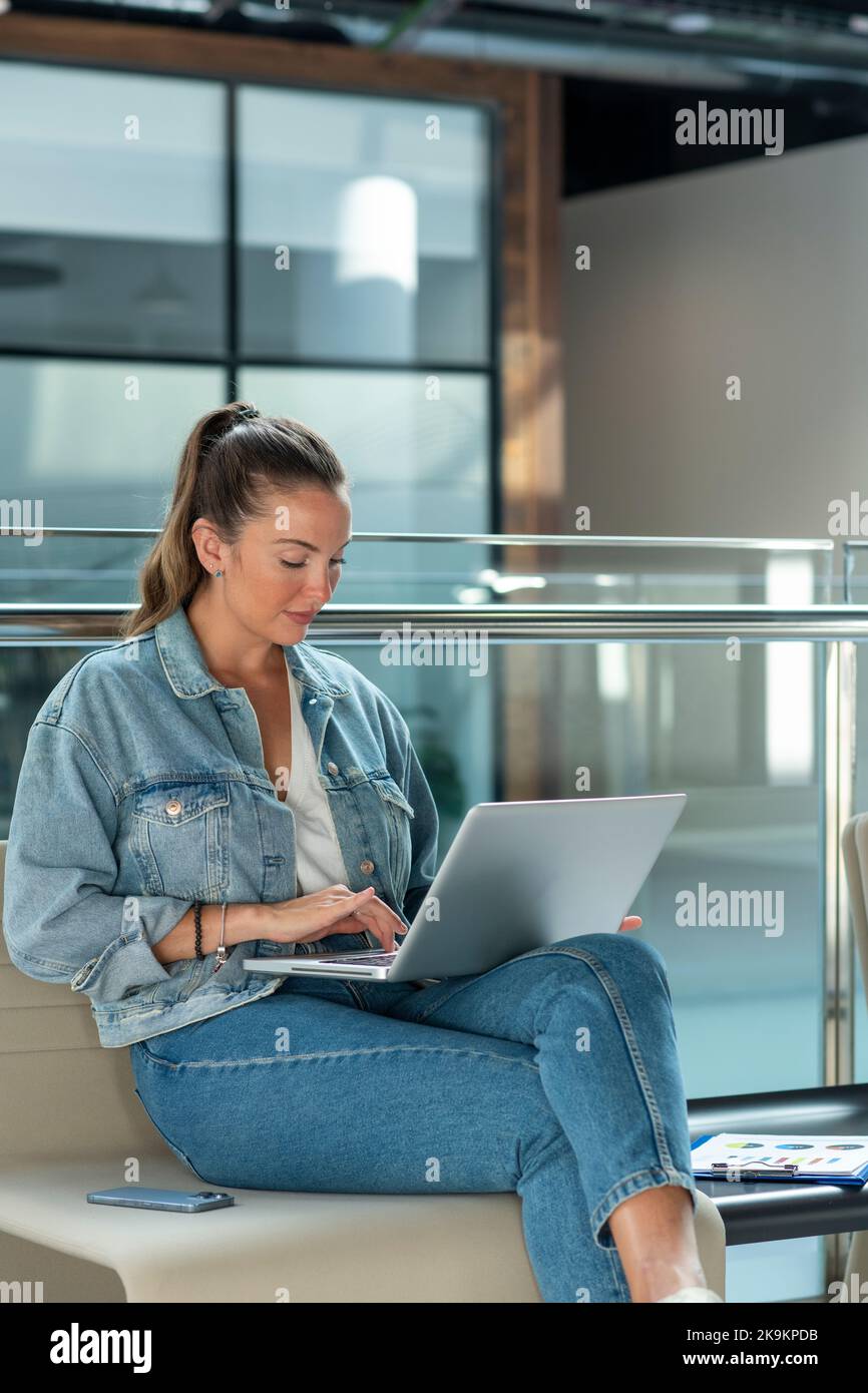 Junge Geschäftsfrau, die im modernen Büro arbeitet, sitzt und mit einem Laptop - Stock photo Stockfoto