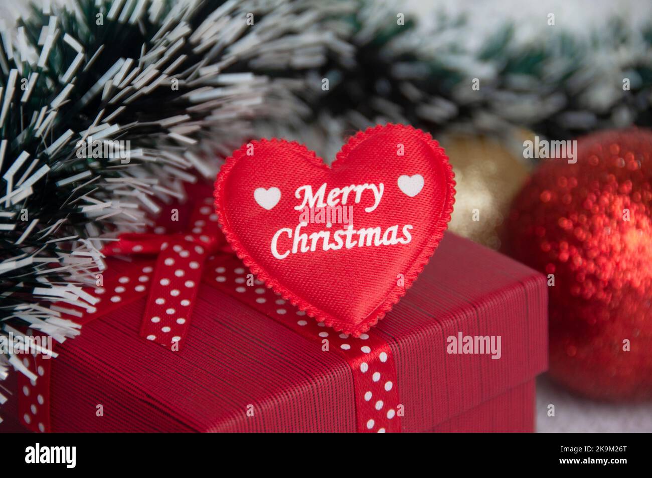 Frohe Weihnachten Text auf Herz-Form auf der Oberseite der roten Farbe Geschenk mit Weihnachtsdekoration Hintergrund. Weihnachtsgeschenk und Festungskonzept. Stockfoto