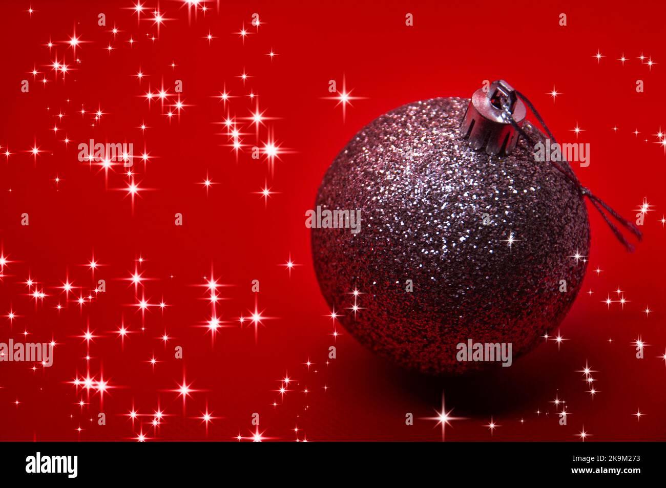 Silberner Weihnachtsball auf rotem Hintergrund, umgeben von leuchtenden Sternen. Weihnachtsfeier Konzept. Stockfoto