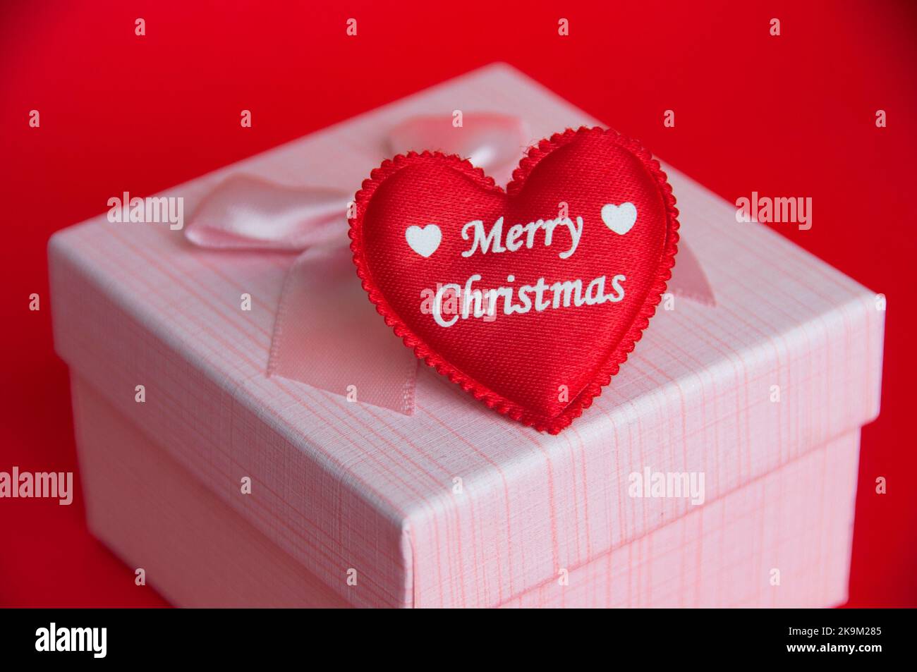 Fröhliche Weihnachten Text auf Herz-Form auf dem Geschenk auf rotem Hintergrund. Weihnachtsgeschenk und Festungskonzept. Stockfoto