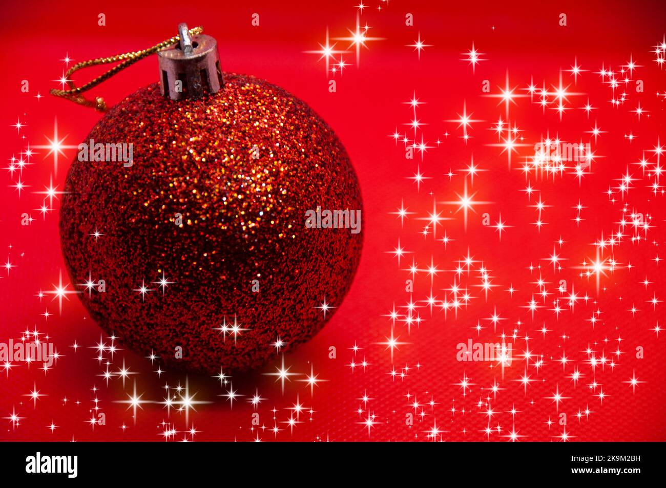 Weihnachtskugel auf rotem Hintergrund, umgeben von leuchtenden Sternen. Weihnachtsfeier Konzept. Stockfoto