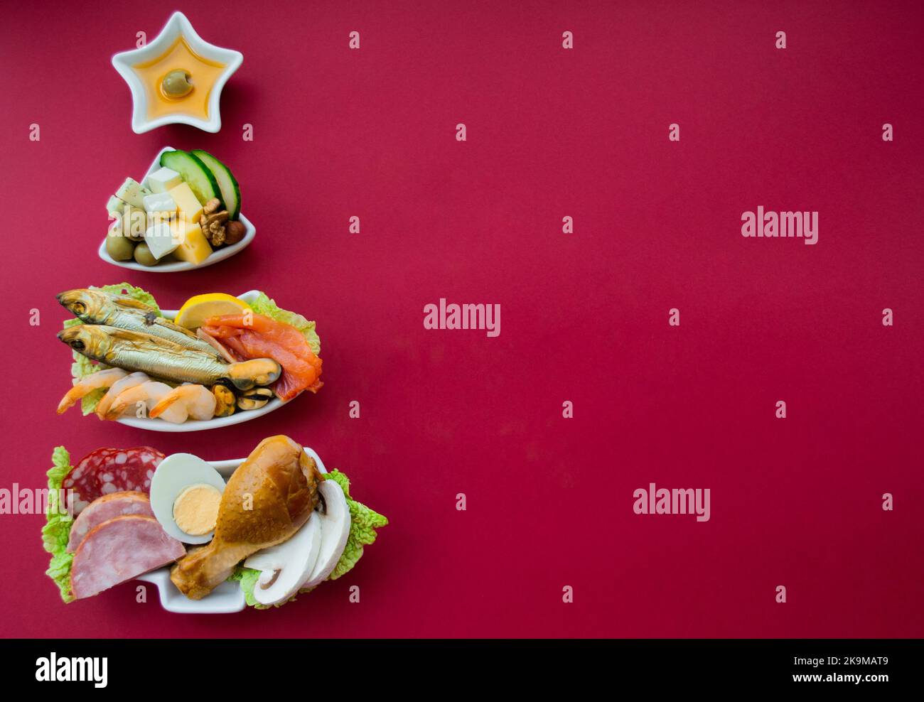 Teller in Form eines Weihnachtsbaums mit Eiweißfutter - Fleisch, Fisch, Käse, Nüsse, etc. Roter Hintergrund. Das Konzept der Keto-Diät behandelt für die holi Stockfoto