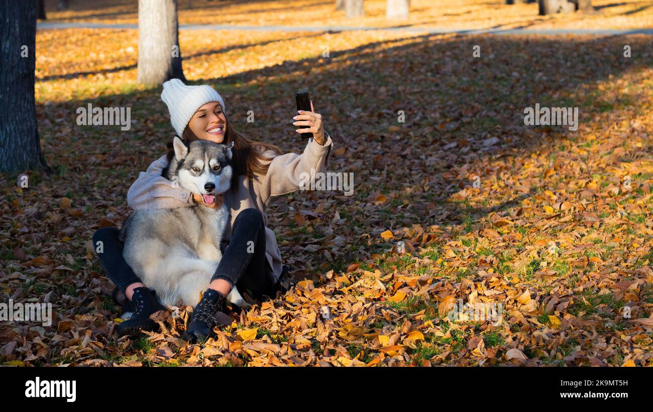 Eine junge Frau umarmt ihren Husky und macht ein Selfie auf einem Smartphone. Moderne Trends in sozialen Netzwerken und aufdringliche Liebe zu Tieren. Stockfoto