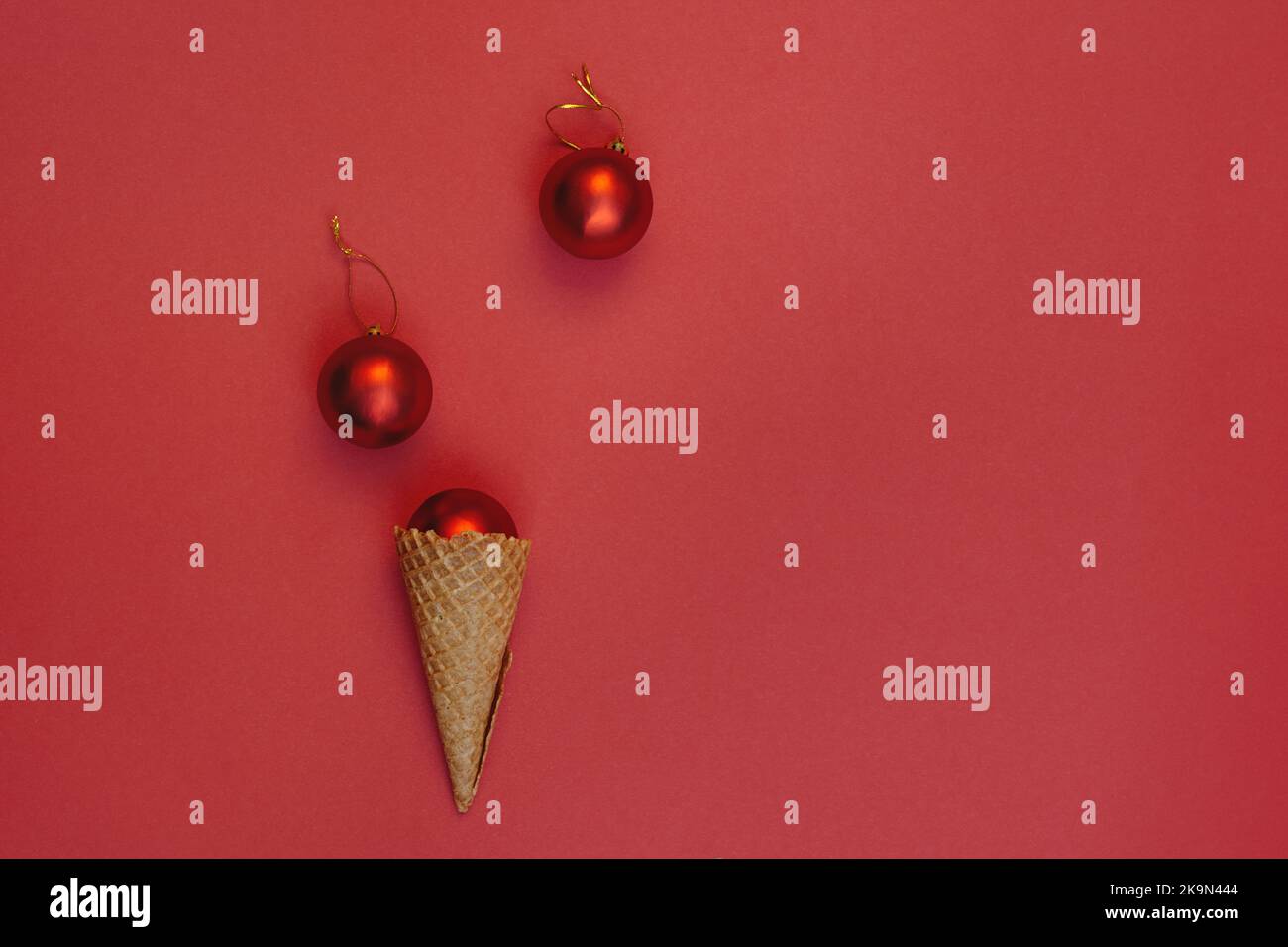 Neujahrskugeln in einem Waffelkegel auf rotem Hintergrund. Runde Spielzeuge mit Goldfaden. Alternative Konzept der Feier Winterferien, top V Stockfoto
