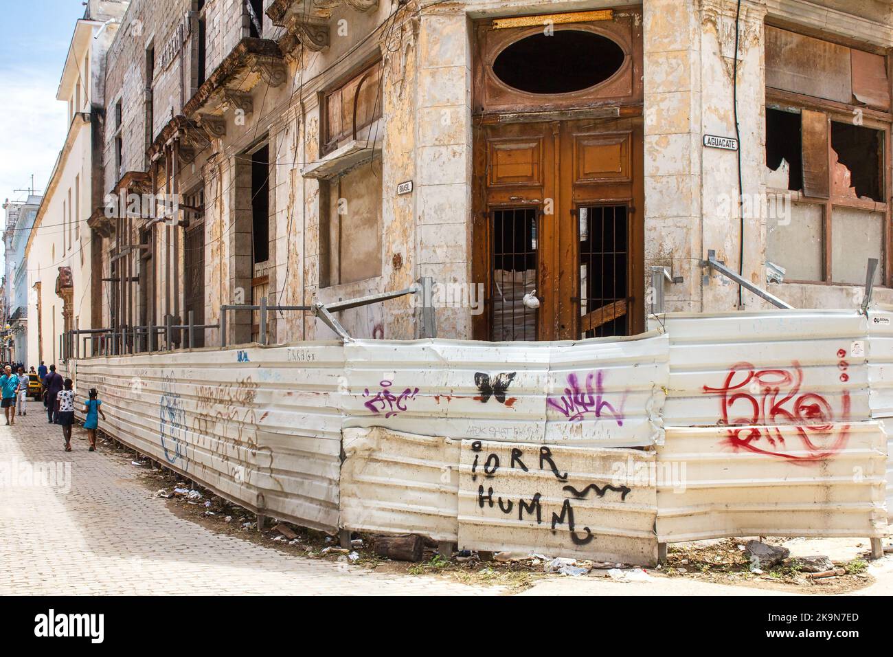 Ein eingestürztes oder heruntergekommenes Gebäude wird durch einen metallischen Zaun geschützt, der mit Graffiti-Markierungen bemalt ist. Stockfoto