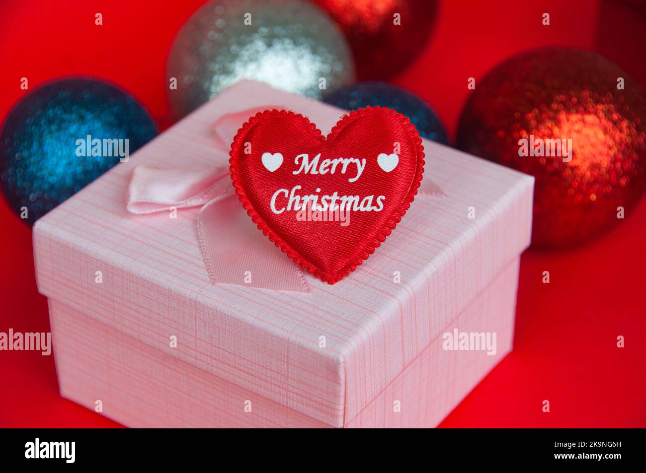 Frohe Weihnachten Text auf Herz-Form auf rosa Farbe Geschenk mit Weihnachtsdekoration Hintergrund. Weihnachtsgeschenk und Copy Space Konzept. Stockfoto