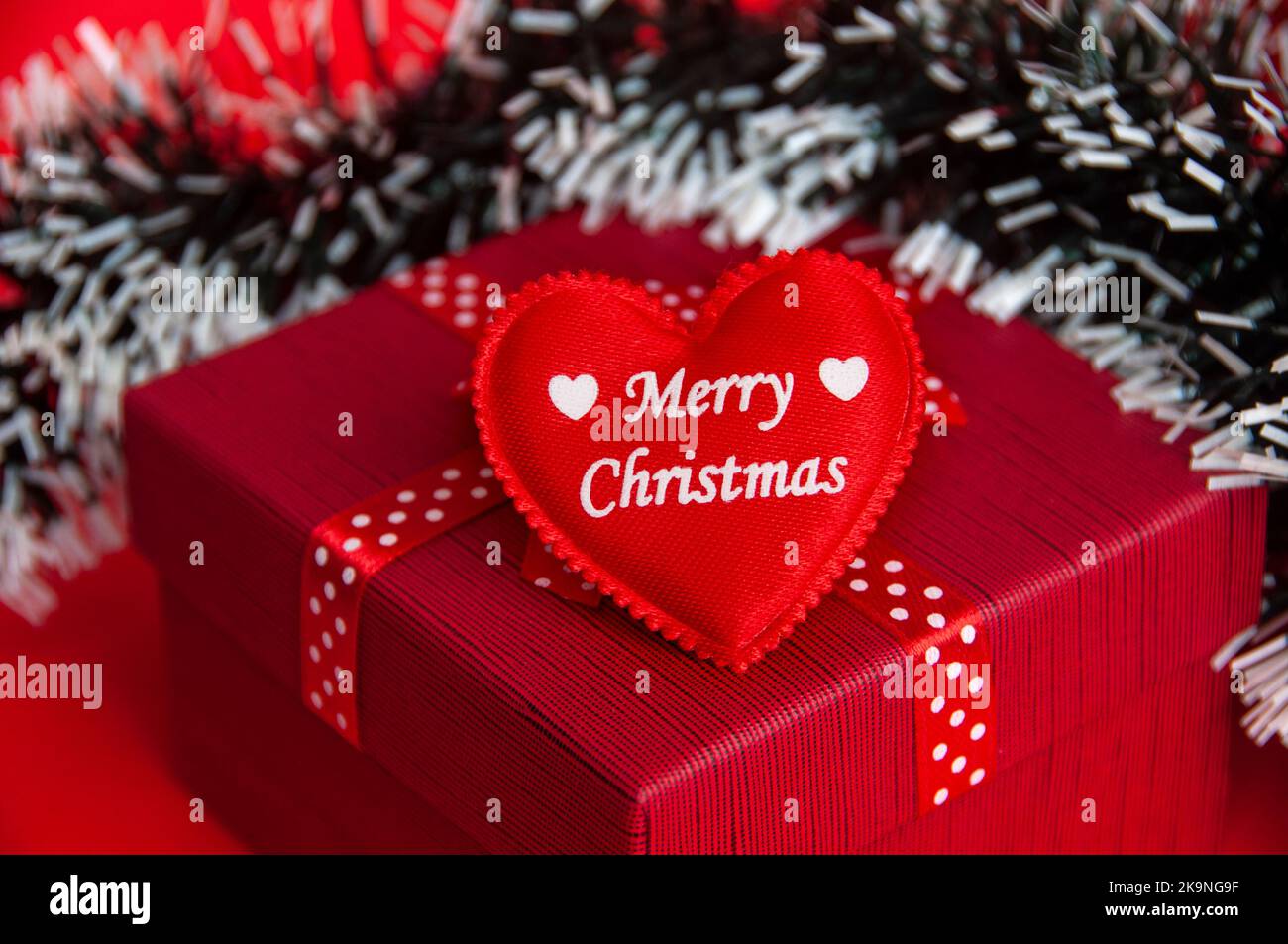 Frohe Weihnachten Textwünsche auf einer Herzform auf der Oberseite der roten Farbe Geschenk mit Weihnachtsdekoration Hintergrund. Stockfoto