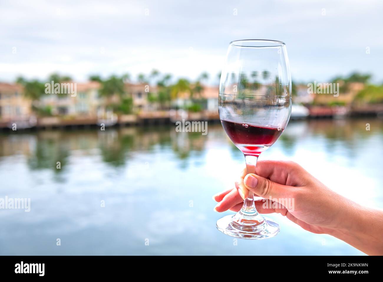 Frau Person Hand halten, Toasten mit Weinglas von Französisch Rotwein Cotes Du Rhone auf Luxus-Haus am Wasser Balkon in Miami, Florida Stockfoto