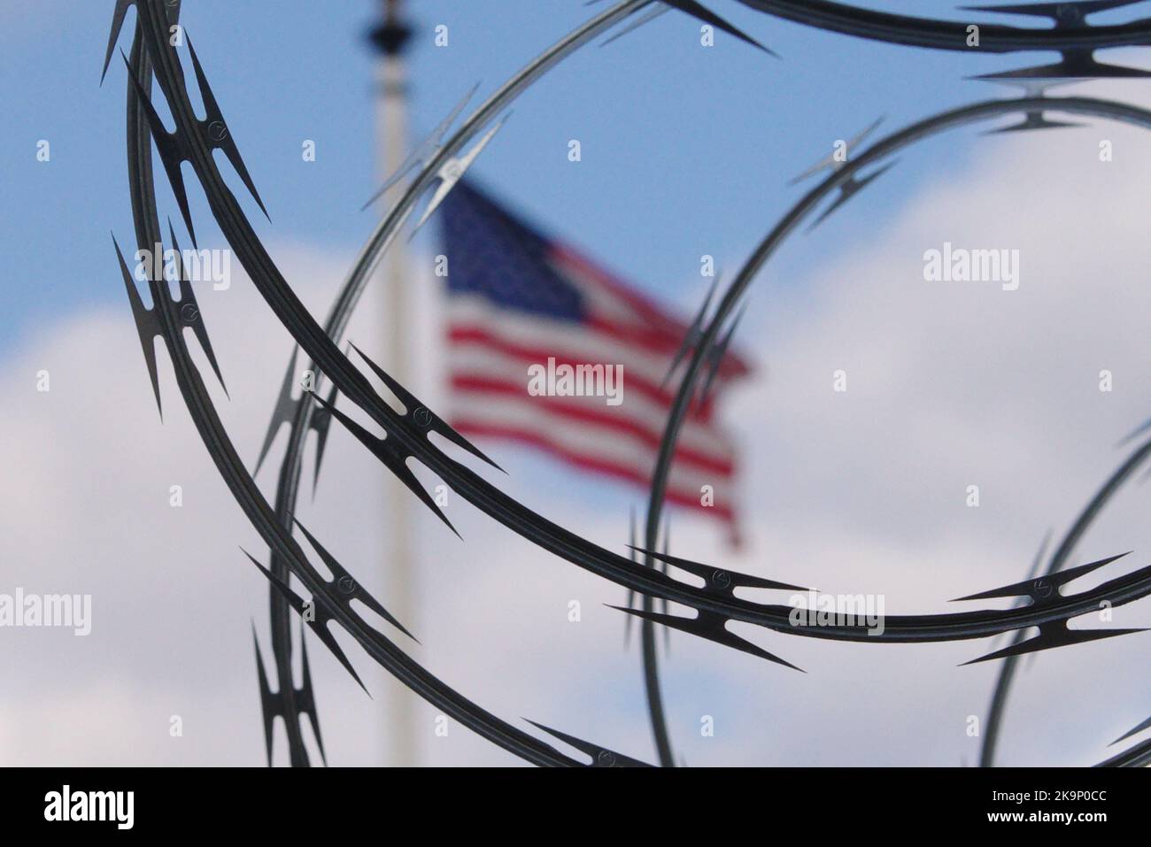 Eine amerikanische Flagge fliegt hinter Stacheldraht, der einen Zaun überragt, der den US-Kapitolkomplex monatelang nach dem Aufstand vom 6. Januar umgab. Stockfoto