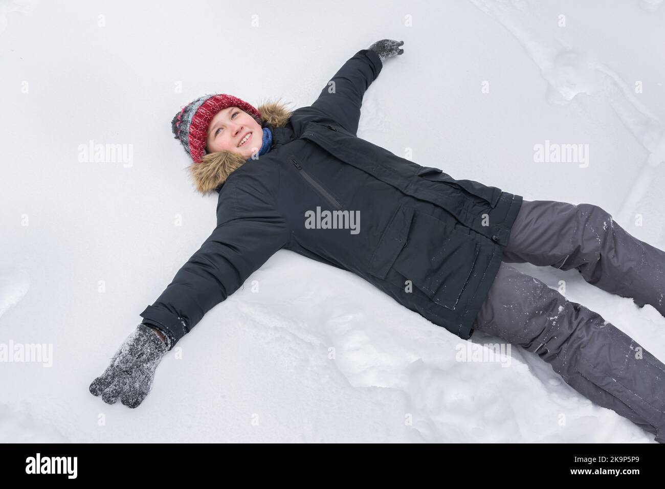 Ein glücklicher Teenager, 12 Jahre alt, liegt im weißen Schnee. Der Winterurlaub Stockfoto