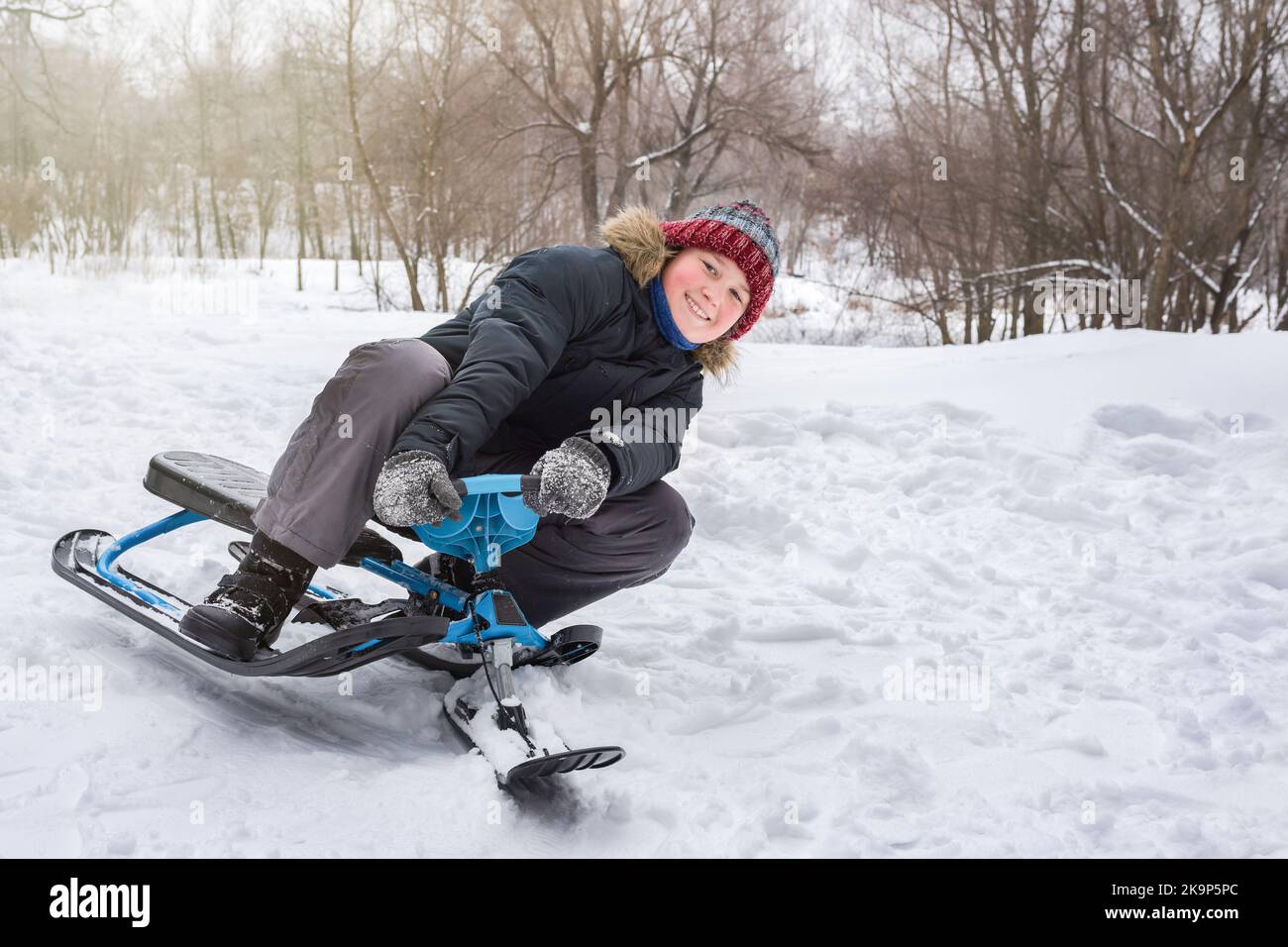 Happy Boy fährt im Winter von einem Berg im Schnee mit einem Schneescooter Stockfoto