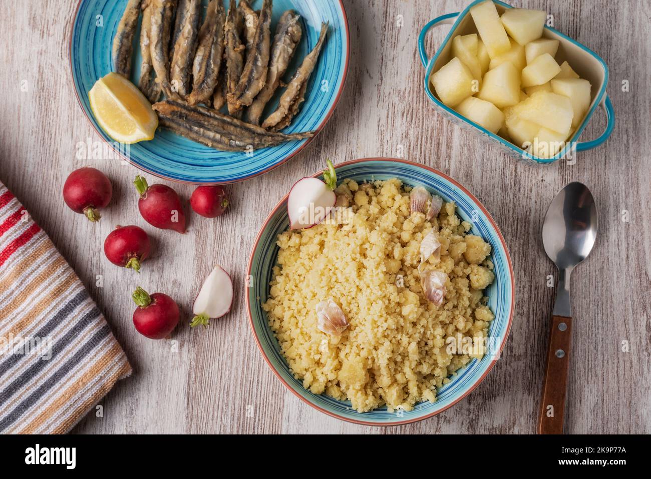 Teller mit Migas, traditionelle spanische Küche, begleitet von Radieschen, Fisch und Melone auf einem Holztisch. Stockfoto