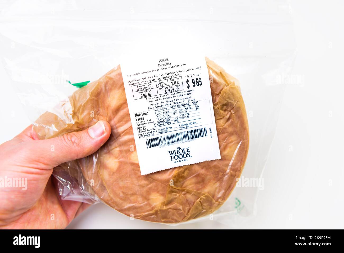 Neapel, USA - 21. Oktober 2021: Hand hält dünne Scheiben Schweinefleisch geheilt italienische Mortadella Wurst bologna von Whole Foods Markt Lebensmittelgeschäft Stockfoto