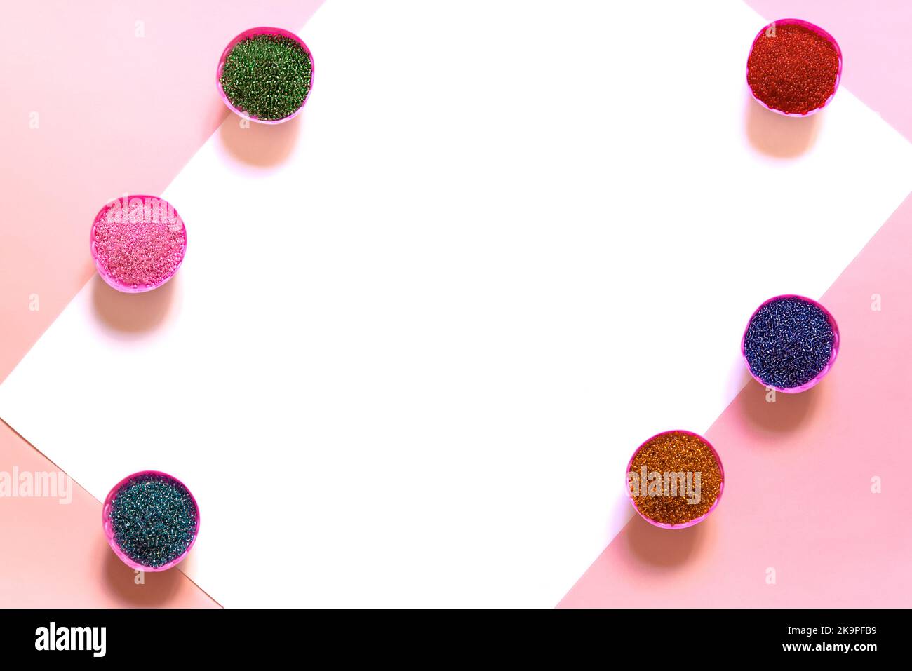 Bunte Glasperlen. Eine Vielzahl von Formen und Farben, um eine Perlenkette oder Kette von Perlen für Frauen zu machen. Box auf rosa und weißem Hintergrund. Ein Regenbogen aus bunten Saatperlen, die zum Perlen bereit sind Stockfoto