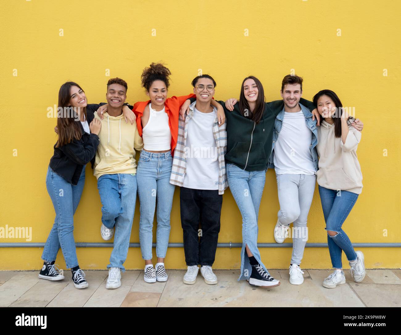 Gruppe junger multiethnischer Freunde, die lachen und die Kamera an einer gelben Wand betrachten. Freundschaft und Diversität Konzept Stockfoto