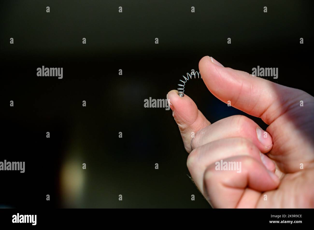 Kaukasische hand Komprimieren einer Metallfeder zwischen Daumen und Finger Stockfoto