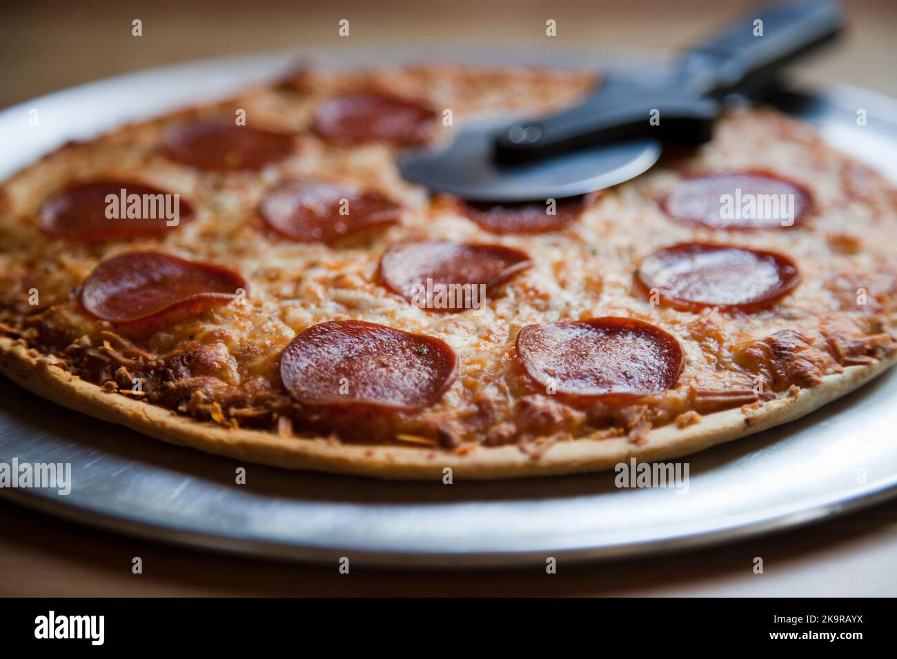 Gebackene Pepperoni- und Käse-Pizza mit dünnem Teig mit einem Pizzaschneider Stockfoto