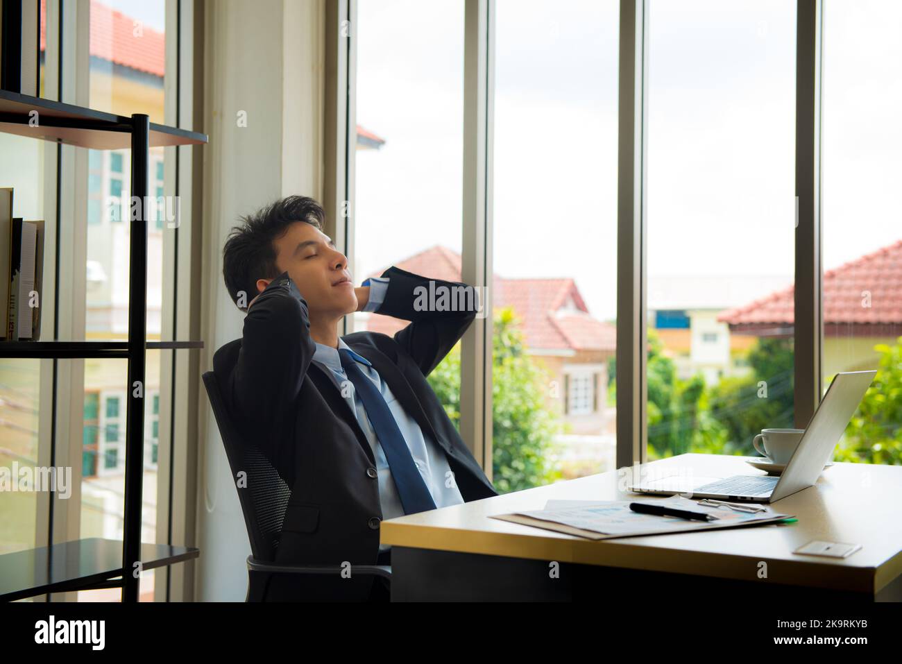 Junger Geschäftsmann, der sich mit den Händen hinter dem Kopf an seinem Schreibtisch im Büro entspannt. Stockfoto