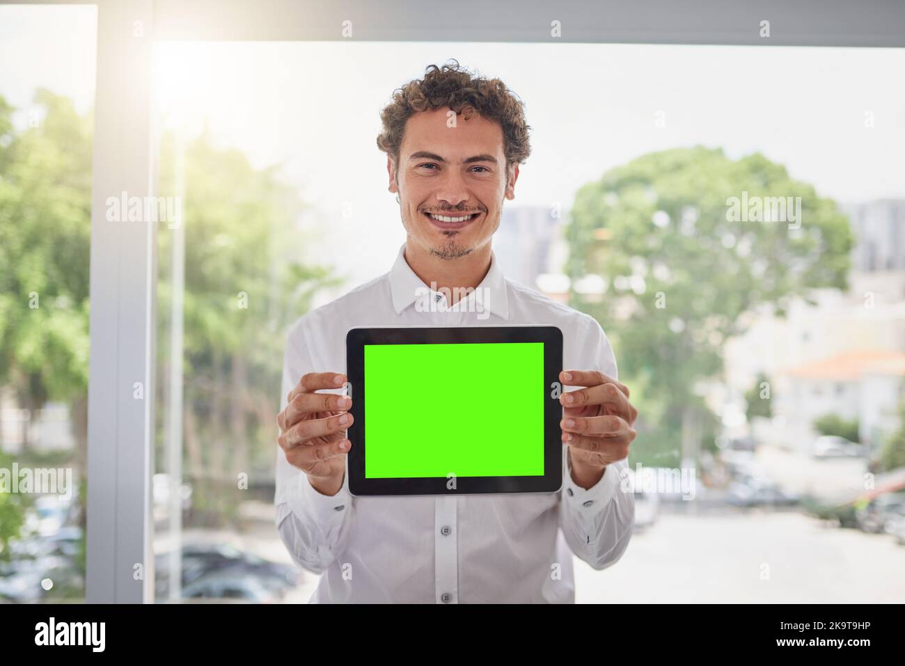 Die ideale App für Ihre geschäftlichen Interessen. Porträt eines hübschen jungen Geschäftsmannes, der ein digitales Tablet mit grünem Bildschirm in einem modernen Büro hält. Stockfoto