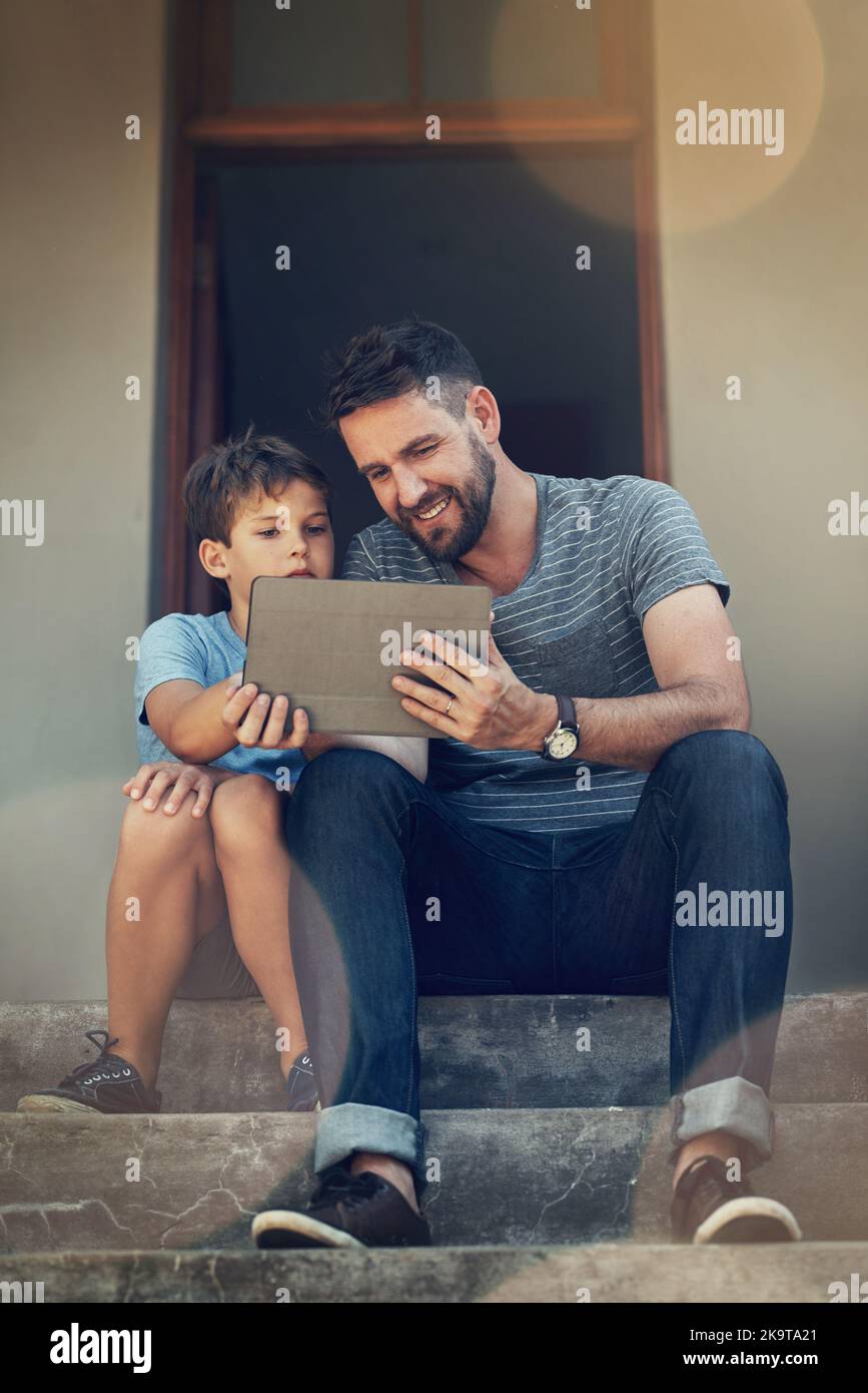Der Lernprozess ist praxisnahe: Ein Vater und ein Sohn nutzen gemeinsam ein digitales Tablet auf den ersten Stufen ihres Zuhauses. Stockfoto