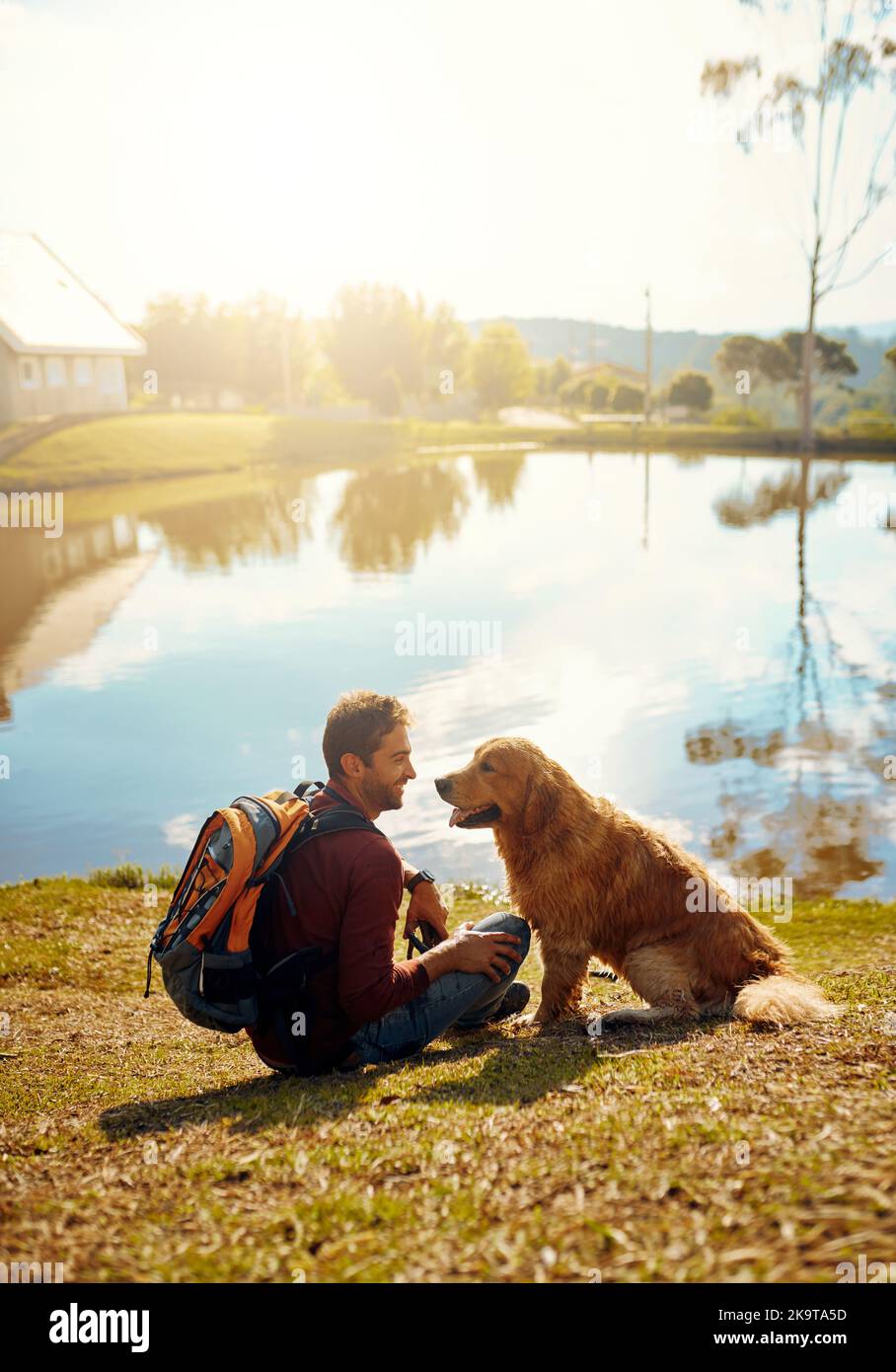 Hes definitiv dieser mans beste Freund. Ganzkörperaufnahme eines hübschen jungen Mannes und seines Hundes, der an einem See im Park sitzt. Stockfoto