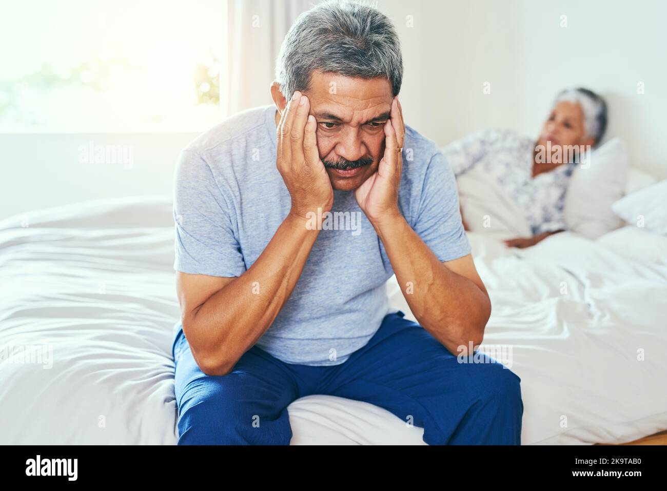 Wir wissen noch heute, wie man argumentiert. Ein gereifter Mann, der auf einem Bett saß und seine Frau im Hintergrund lag, nachdem sie zu Hause gestritten hatten Stockfoto