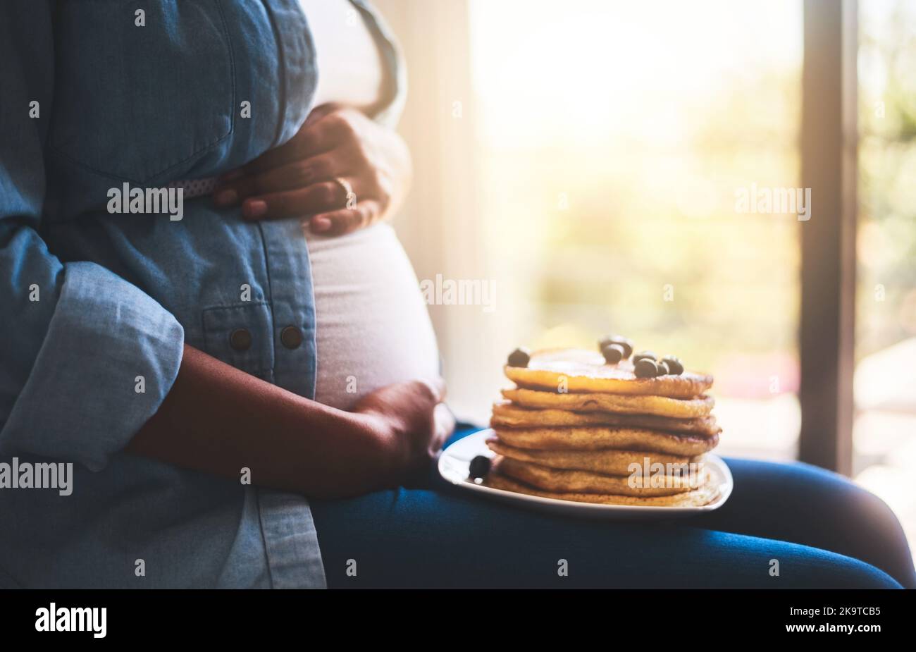 Beginnen Sie den Morgen mit etwas Süße. Eine Schwangerin, die zu Hause leckere Pfannkuchen isst. Stockfoto