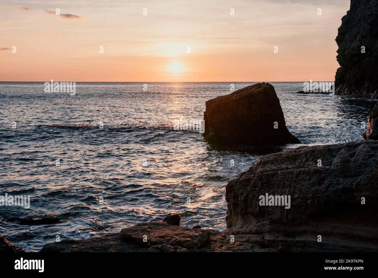 Blick auf den Sonnenuntergang auf das ruhige Meer und die vulkanischen felsigen Küsten. Kleine Wellen o Stockfoto