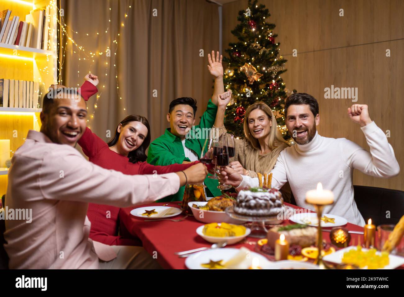 Verschiedene Freunde lächeln und betrachten Kamera Gruppe von Menschen feiern Neujahr und Weihnachten zu Hause sitzen am Weihnachtsessen und Wein trinken, Porträt von glücklichen Menschen an Feiertagen. Stockfoto