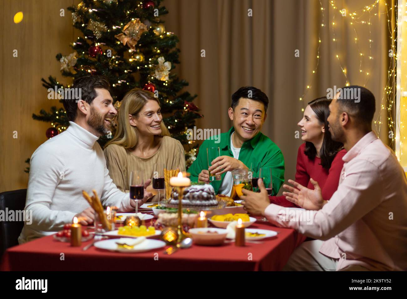 Freunde feiern Weihnachtsabend oder Silvester paty zusammen am Tisch sitzen. Schlemmen Sie zu Hause Gruppe von multi ethnischen festlichen weihnachtsessen. Glückliche fröhliche Menschen. Stockfoto