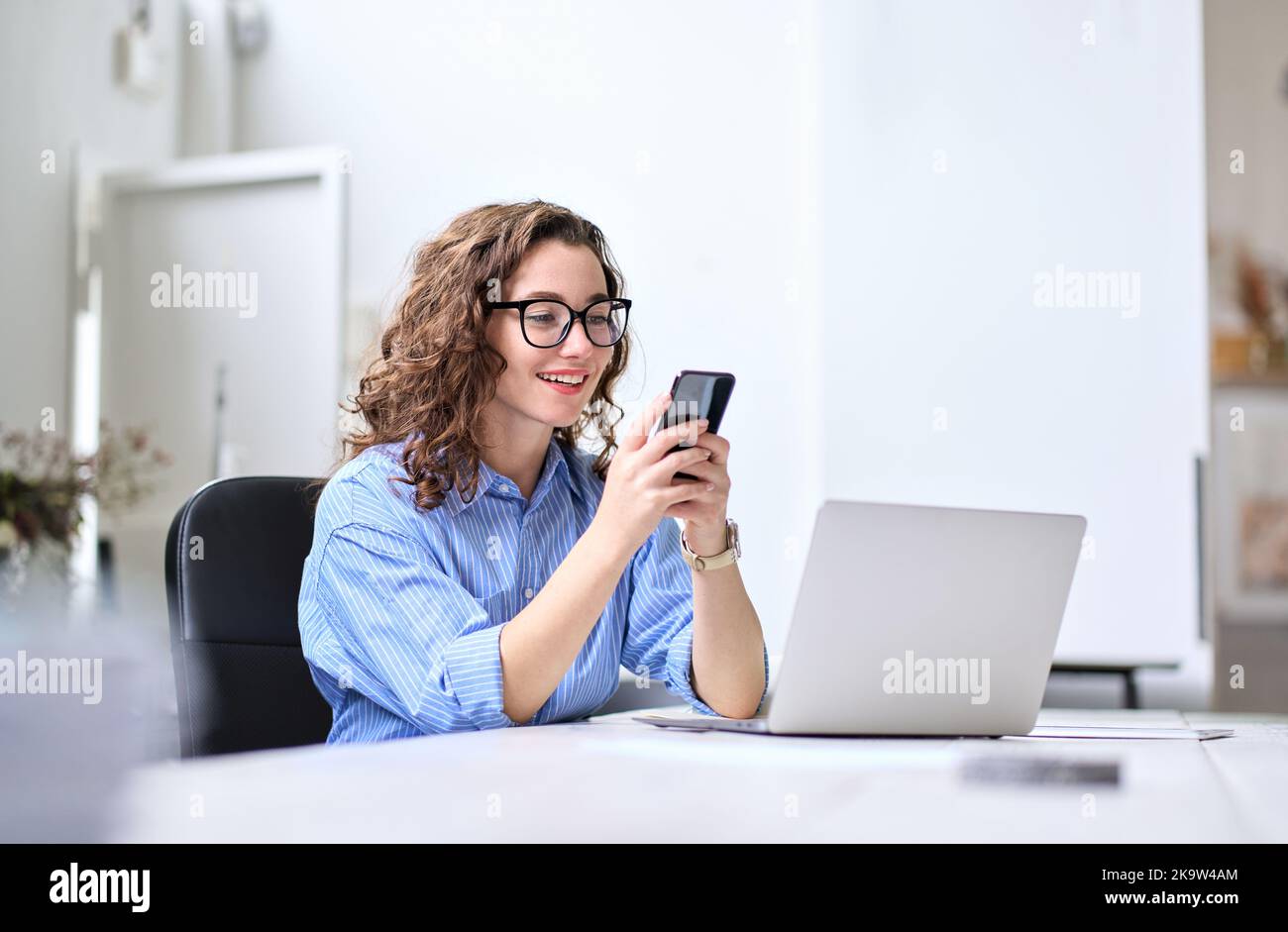 Glückliche junge Geschäftsfrau, die im Büro am Schreibtisch mit dem Handy arbeitet. Stockfoto