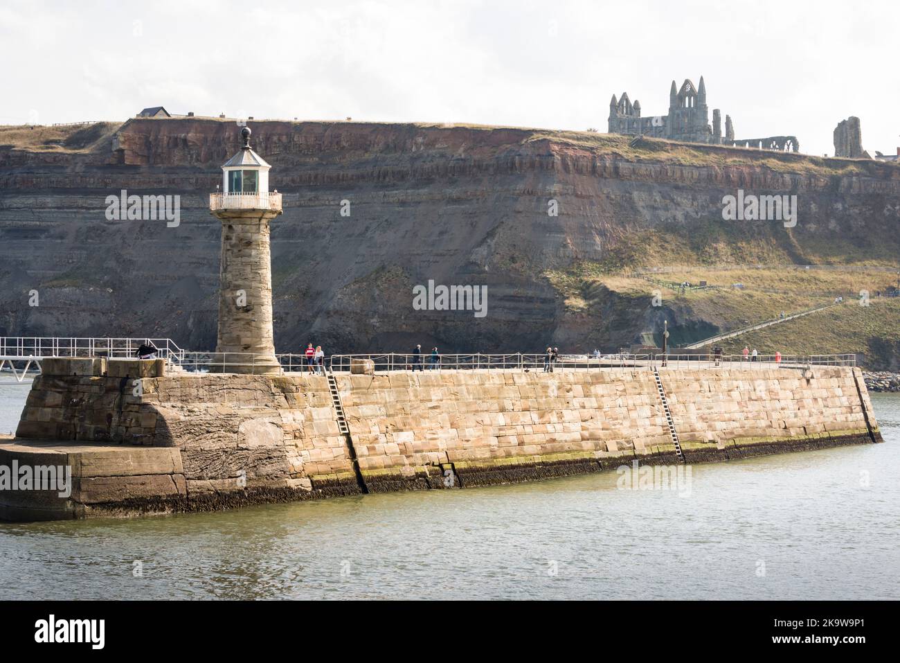 WHITBY, Großbritannien - 21. September 2022. Whitby Hafenmauer mit Leuchtturm. Whitby Abbey Ruinen im Hintergrund. Stockfoto