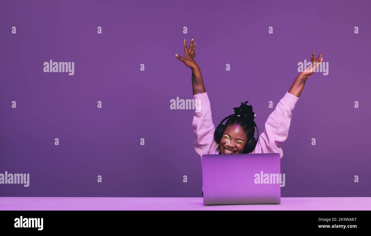 Glückliche Gamer feiert den Gewinn eines Videospiels in einem Studio. Fröhliche junge Frau, die ein Online-Spiel mit einem Laptop und Headsets spielt. Junge Frau s Stockfoto