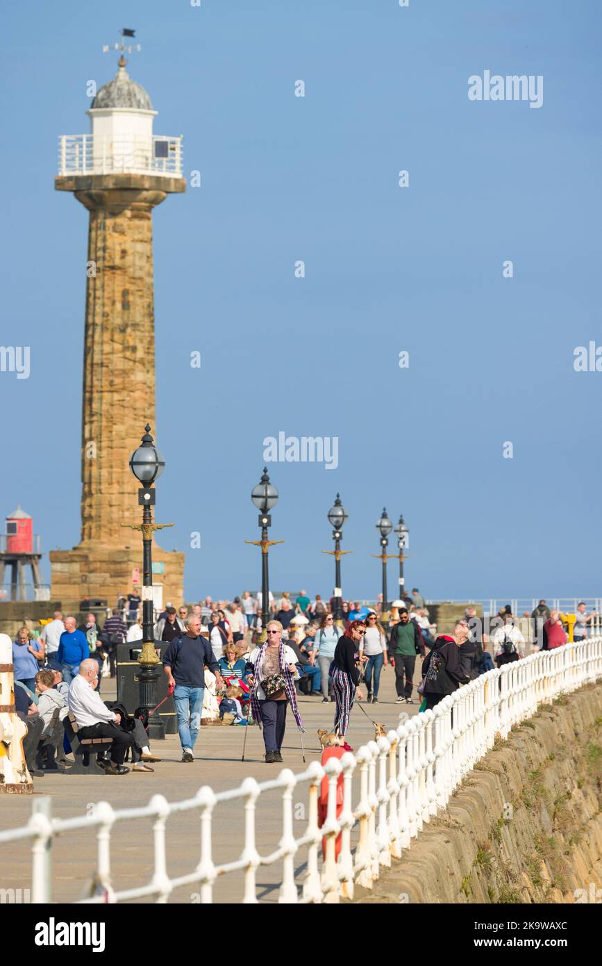 WHITBY, Großbritannien - 21. September 2022. Touristen laufen entlang Whitby Pier (Hafenmauer) mit einem Leuchtturm im Hintergrund. Whitby, North Yorkshire, Großbritannien Stockfoto