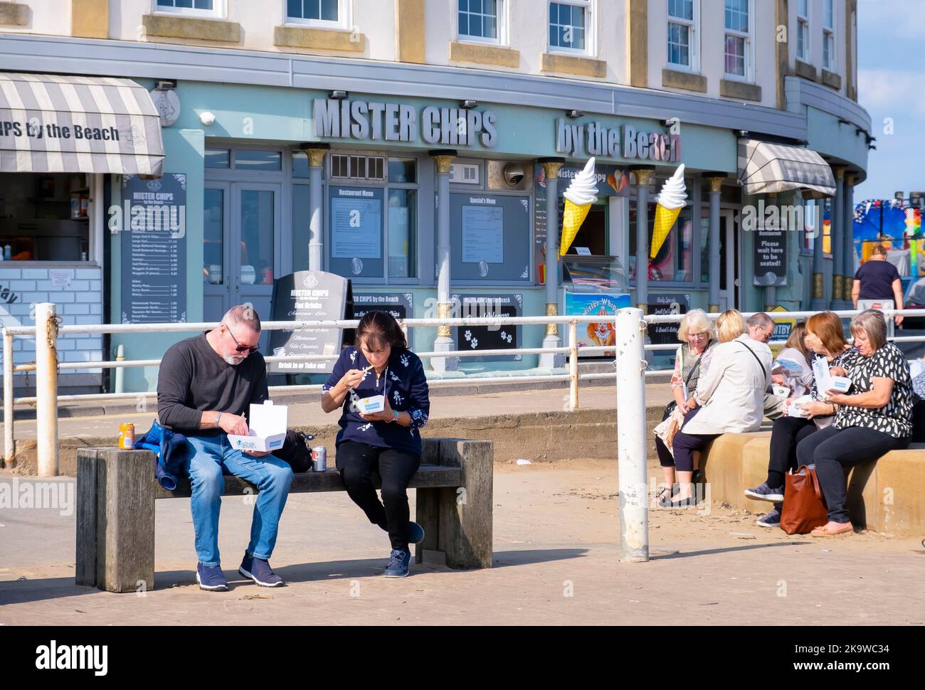 WHITBY, Großbritannien - 21. September 2022. Menschen, die auf einer Bank vor einem Fish and Chip Shop in Whitby Harbour, North Yorkshire, Fisch und Chips essen Stockfoto