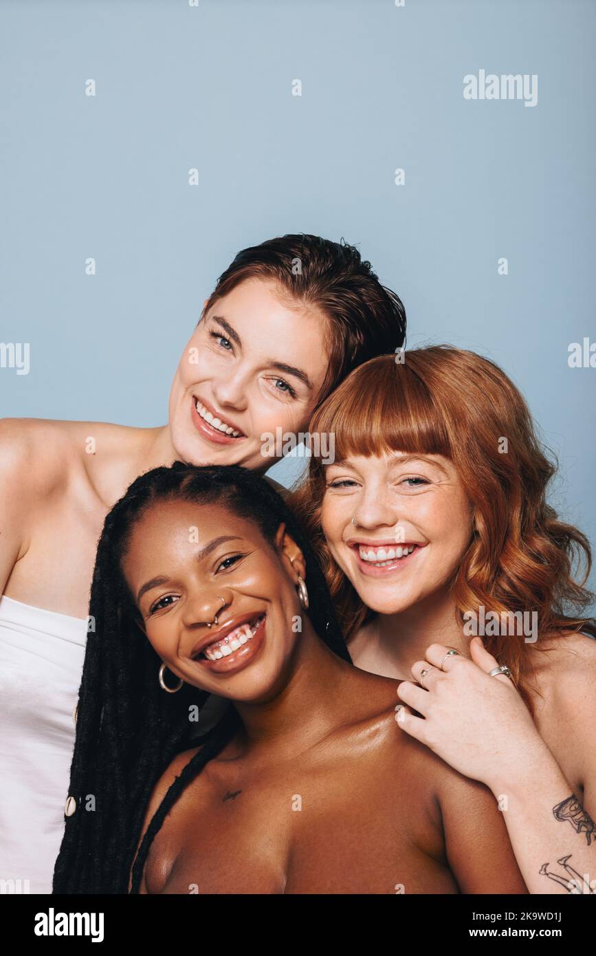 Glückliche Frauen mit unterschiedlichen Hauttönen lächeln in einem Studio an der Kamera. Gruppe von körperbewussten jungen Frauen umarmen ihre natürliche Schönheit. Drei bsb Stockfoto