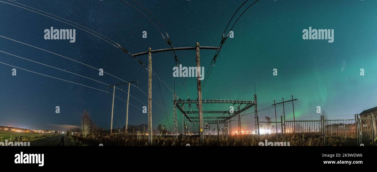 Schönes, breites Nachtpanorama mit Aurora über einem elektrischen Umspannwerk und hölzernen Pol-Stromleitungen, Sternenhimmel mit Aurora Borealis. Schweden, Umea Stockfoto